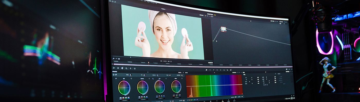 Back view of a young white man video editor sitting in front of a big screen working on a video montage indoors