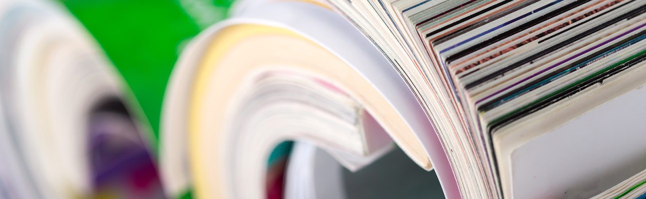 Colorful magazines are rolled and placed on a flat surface showing parts of their covers.